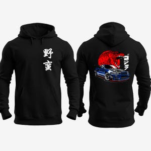 May include: Black hooded sweatshirt with white Japanese characters on the front. The back features a blue sports car graphic with a red sun and Japanese text. A stylish and comfortable apparel item.