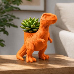 Könnte beinhalten: Ein leuchtend orangefarbener, dinosaurierförmiger Übertopf mit strukturierter, schuppiger Oberfläche und einer breiten Öffnung auf dem Rücken. Eine leuchtend grüne Sukkulente mit spitzen, geschichteten Blättern steht in der Höhlung der Figur.