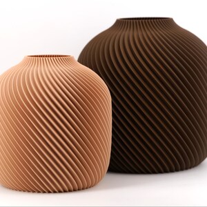 Könnte beinhalten: Zwei dekorative Vasen mit einem Spiraldesign. Eine Vase ist hellpfirsichfarben, die andere dunkelbraun. Die Vasen haben eine abgerundete Form mit einer schmalen Öffnung oben. Das Spiralmuster erzeugt eine strukturierte Oberfläche.