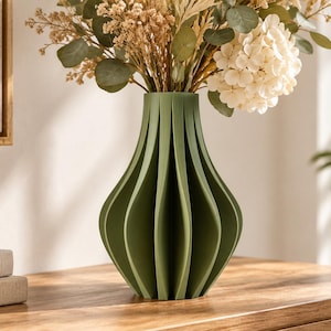 May include: A matte olive green vase with a vertical ribbed, accordion-like structure and a wide, rounded body that tapers toward the top opening, filled with a bouquet of dried beige hydrangeas and green eucalyptus leaves.