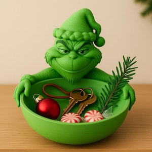 Könnte beinhalten: Eine leuchtend grüne Dekoschale mit einer modellierten Grinch-Figur, die mit einer passenden Mütze den Rand hält. Die Schale enthält eine kleine rote Kugel, zwei Metallschlüssel an einer braunen Lederschlaufe, zwei Pfefferminzbonbons und einen Tannenzweig.