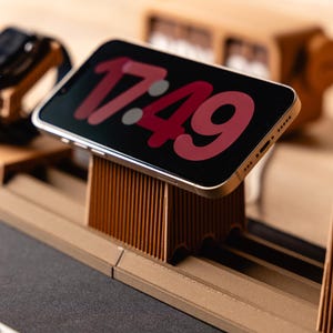 May include: A brown, ribbed, 3D-printed desk organizer set featuring a central smartphone stand displaying the time 17:49 on its screen, a side watch holder, and a pen cup, all arranged on a modular, tiered base with a linear, vertical texture.