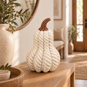 Peut inclure: Un objet décoratif en forme de citrouille présentant une surface texturée composée de crêtes verticales torsadées ressemblant à de la corde, de couleur blanc cassé. Le sommet est doté d'une tige incurvée marron lisse imitant un pédoncule.
