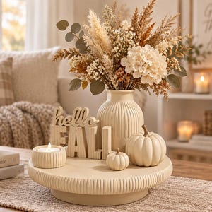 Könnte beinhalten: Ein cremefarbenes Dekotablett mit einer gerippten Vase voller Trockenblumen, zwei weißen Kürbissen, einer kleinen Kerze in einem gerippten Halter und einem Holzschild mit dem Text hello FALL, arrangiert auf einem Tisch.