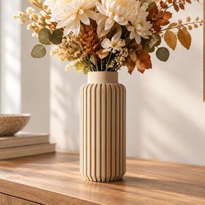 May include: A cylindrical vase with a light beige finish and a vertical ribbed texture. The vase is filled with a bouquet of dried flowers in shades of cream, tan, and brown, featuring large petals, small clusters, and round green eucalyptus leaves.