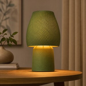 Op de afbeelding: Een tafellamp met een getextureerde, olijfgroene mesh kap en een bijpassende cilindrische voet. De lamp verspreidt een warme, zachte gloed van binnenuit en verlicht het oppervlak eronder. Het ontwerp bestaat uit een breed, taps toelopend bovendeel.