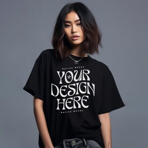 Pu&ograve; includere: Una maglietta nera con una grafica bianca che dice "YOUR DESIGN HERE" e "NATIVE MOCKS" sopra e sotto il testo. La maglietta &egrave; indossata da una persona con i capelli scuri.