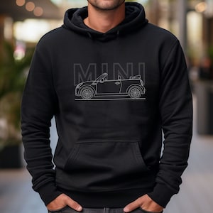 Puede incluir: Una sudadera con capucha negra con un contorno blanco de un Mini Cooper descapotable y la palabra "MINI" impresa en la parte delantera.