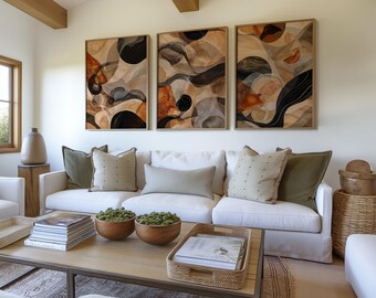 Könnte beinhalten: Drei abstrakte Kunstdrucke mit braunen, schwarzen und weißen geometrischen Formen und Wirbeln. Die Drucke sind in Naturholz gerahmt und an einer weißen Wand über einem weißen Sofa mit grünen und beigen Kissen aufgehängt.