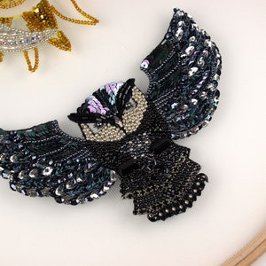 May include: A black and silver beaded owl with iridescent wings. The owl is a decorative piece and is made of beads and sequins.