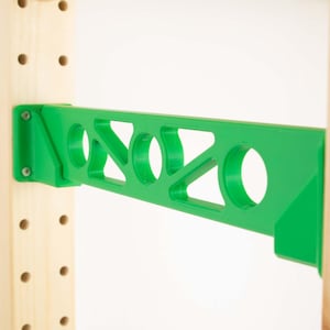 May include: A bright green shelf bracket with a geometric design, mounted on a wooden support. The bracket features circular and triangular cutouts, and is secured with screws. The design is modern and functional.