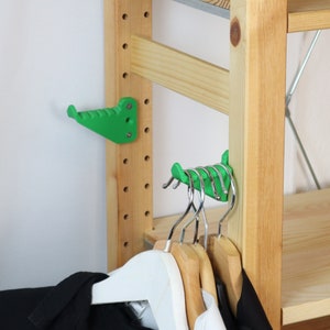 Può includere: Ganci in plastica verde montati su uno scaffale in legno con appendiabiti appesi.