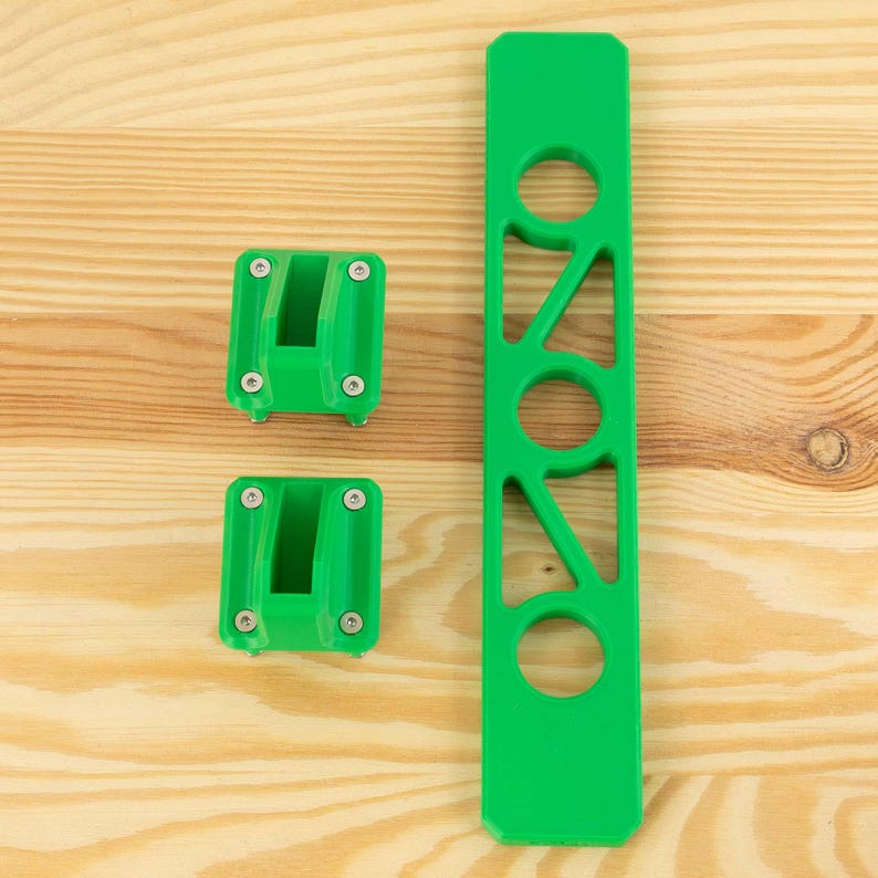 May include: Bright green mounting brackets and a long, slotted piece. The brackets have a U-shaped design with screws. The long piece has cut-out circles and angles. All pieces are made of a solid, opaque material.
