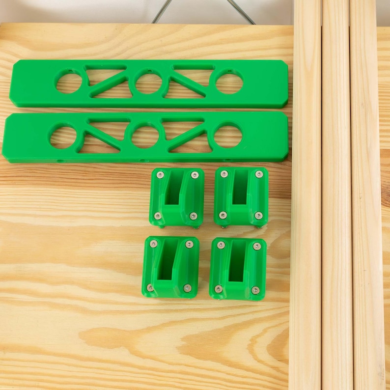 May include: A collection of green plastic components and wooden dowels, likely for furniture assembly. The green pieces include two long bars with circular and angled cutouts, and four square brackets. The wooden dowels are light brown.