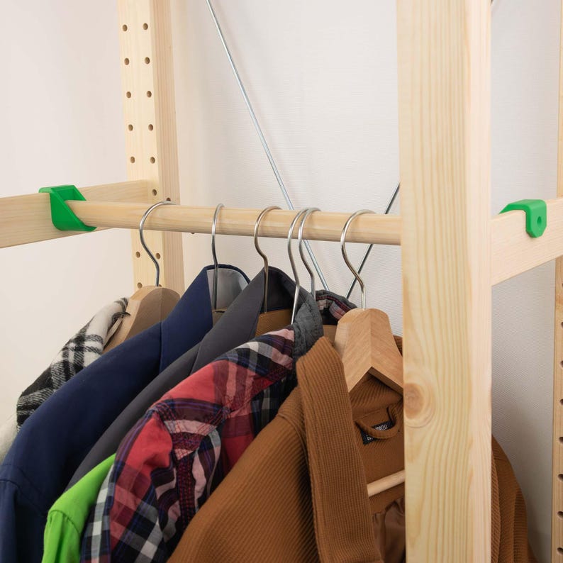 May include: A wooden clothing rack with various jackets and shirts hanging on metal hangers. The jackets include a navy blue blazer, a red plaid shirt, and a brown corduroy jacket. Green plastic clips secure the wooden rods.