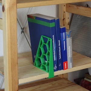 Könnte beinhalten: Ein grüner Buchstützer aus Kunststoff mit einem Wabenmuster hält drei Bücher auf einem Holzregal. Die Bücher sind betitelt "Tabellenbuch Kunststofftechnik", "Tabellenbuch Metall" und "Technische Formelsammlung".