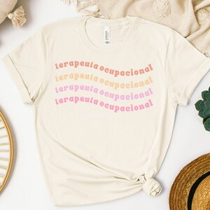 May include: A beige t-shirt with the text "terapeuta ocupacional" repeated four times in a rainbow gradient of pink, orange, and yellow.