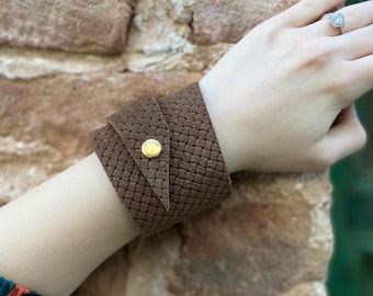 May include: A brown leather cuff bracelet with a woven texture and a gold button closure.