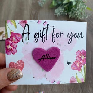 May include: A gift card with the text "A gift for you" and a pink heart with the name "Allison". The card has a floral design with pink flowers and watercolor-style splashes.