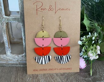 May include: A pair of geometric earrings with a zebra print, red, pink and green leather accents. The earrings are made of real leather and have gold-tone hooks. The earrings are displayed on a brown card with the text "Rose & Leaves" and "Real Leather Jewellery & Accessories".
