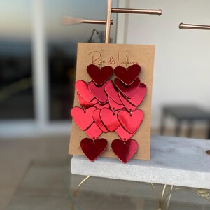 Shiny red leather heart dangle earrings crafted in multiple layers for a unique and lightweight statement look.