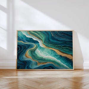 Könnte beinhalten: Abstrakter Kunstdruck mit fließendem Design in Türkis, Blaugrün und Gold. Das Kunstwerk ist in einem hellen Holzrahmen gerahmt und erinnert an das Meer. Das Stück wird vor einer weißen Wand und einem Holzboden präsentiert.