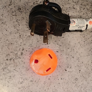 May include: A black electrical plug with a warning label and a bright orange plastic cover for an electrical outlet.