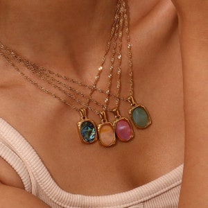 May include: A gold chain necklace with five different oval-shaped pendants. The pendants are made of iridescent abalone shell, pink, peach, and green glass.