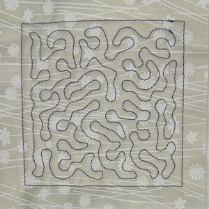 May include: Square fabric piece with a light green background and a white floral and line pattern. A dark blue stitched design of abstract shapes is centered on the fabric. The edges are also stitched in dark blue.