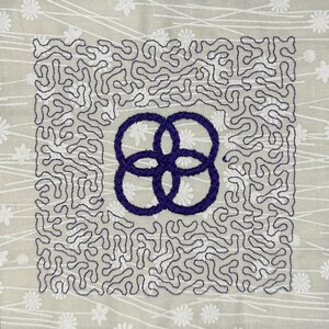 May include: A square embroidery design with a purple interlocking circle pattern in the center. The background is a white fabric with a subtle floral pattern.