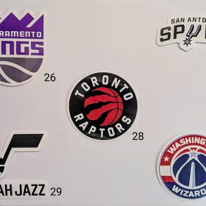 May include: A collection of ten NBA team logos, including the Sacramento Kings, San Antonio Spurs, Toronto Raptors, Utah Jazz, and Washington Wizards. Each logo is a sticker with a number underneath.