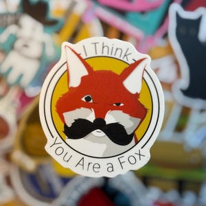 May include: A sticker featuring a cartoon fox with a black mustache and the text "I Think You Are a Fox." The fox is red and white, set against a yellow circle with a white border. The sticker is surrounded by other colorful stickers.