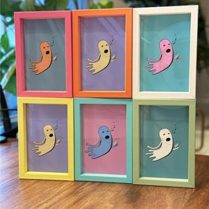 Könnte beinhalten: Sechs farbige gerahmte Kunstdrucke mit einem Cartoon-Oktopus, der ein Surfbrett hält. Die Rahmen sind rosa, orange, weiß, gelb, blau und grün. Der Oktopus ist in verschiedenen Farben vor passendem Hintergrund.
