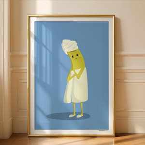 Puede incluir: Una impresión artística enmarcada que presenta un plátano de dibujos animados envuelto en una toalla blanca y con un turbante blanco. El plátano tiene una expresión triste y está sobre un fondo azul. El marco es dorado.
