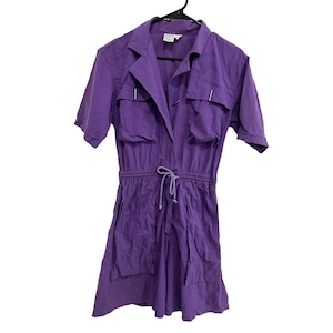 May include: A purple short-sleeved jumpsuit with a collared neckline, two flap pockets on the chest, and a drawstring waist.