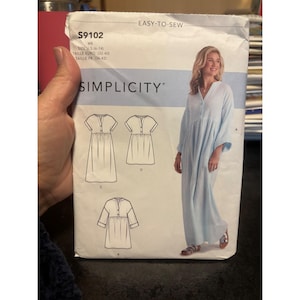 May include: A Simplicity sewing pattern, S9102, featuring a light blue dress with short sleeves and a button-down front. The pattern includes size options from 6 to 14. The words "Easy-to-Sew" and "Simplicity" are printed on the pattern.