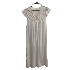 May include: A white floor-length nightgown featuring short flutter sleeves, a V-neckline with thin tie closures, and delicate pink and blue floral embroidery detailing across the chest area. The garment hangs from a black plastic hanger.