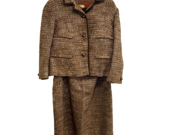 May include: A vintage brown tweed skirt suit. The jacket has a notched collar, three buttons, and two front pockets. The skirt is knee-length. The suit is hanging on a black hanger against a white background.