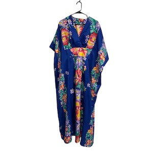 May include: A floor-length kaftan dress in a vibrant royal blue featuring a colorful tropical floral print with red, yellow, and pink hibiscus flowers and green palm leaves. The garment has a V-neckline, short sleeves, and a gathered waistline.