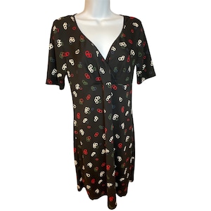 May include: A black knee-length dress with short sleeves and a V-neckline. The fabric features a repeating pattern of small, interconnected circular links in white, red, and dark green colors distributed across the entire garment surface.