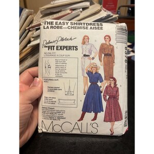 Może przedstawiać: Zabytkowy wzór krawiecki McCall's na koszulową sukienkę. Wzór zawiera ilustracje różnych stylów sukienek koszulowych w różnych kolorach. Tekst na wzorze brzmi "The Easy Shirtdress" i "Palmer/Pletsch The Fit Experts".