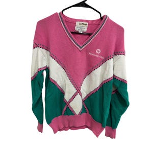 May include: A V-neck sweater featuring a color-blocked design in pink, white, and teal. The front displays a geometric diamond pattern with thin black lines and the embroidered text Pentastar Club with a star logo on the upper right chest area.
