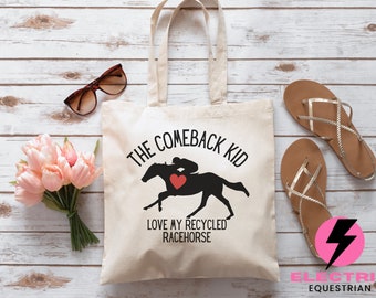 May include: Cream-colored tote bag with the text "THE COMEBACK KID" above a black silhouette of a racehorse and jockey with a red heart. The text "LOVE MY RECYCLED RACEHORSE" is below the image. Sunglasses, pink flowers, and sandals are also in the image.