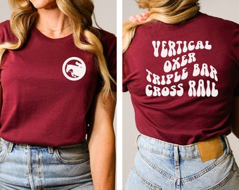 May include: A maroon t-shirt with a white horse graphic on the front and the text "VERTICAL OXER TRIPLE BAR CROSS RAIL" in a retro font on the back.