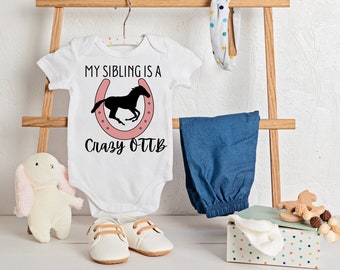 May include: White baby onesie with the text "My sibling is a crazy OTTB" and a pink horseshoe with a black silhouette of a horse running inside.