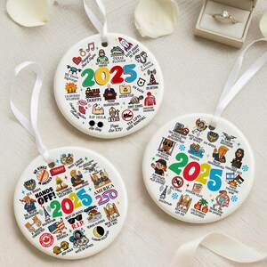 May include: Three white ceramic ornaments with white ribbons. Each ornament features the year "2025" in colorful text, surrounded by small illustrations and text. The ornaments are likely commemorative or decorative items.