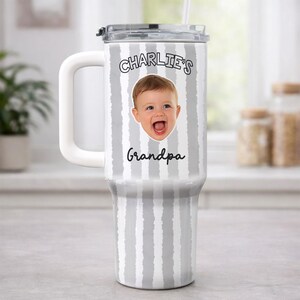 K&ouml;nnte beinhalten: Ein gro&szlig;er, wei&szlig;-grau gestreifter Becher mit wei&szlig;em Griff und transparentem Deckel. Der Becher zeigt ein Foto eines Babys und den Text "Charlie's Grandpa" in schwarzer Schrift.