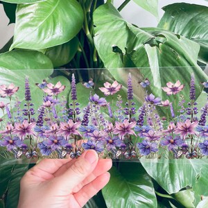 Puede incluir: Una l&aacute;mina transparente de vinilo con un dise&ntilde;o impreso de flores moradas y rosas y mariposas. Las flores est&aacute;n dispuestas en fila y las mariposas est&aacute;n dispersas por todo el dise&ntilde;o.