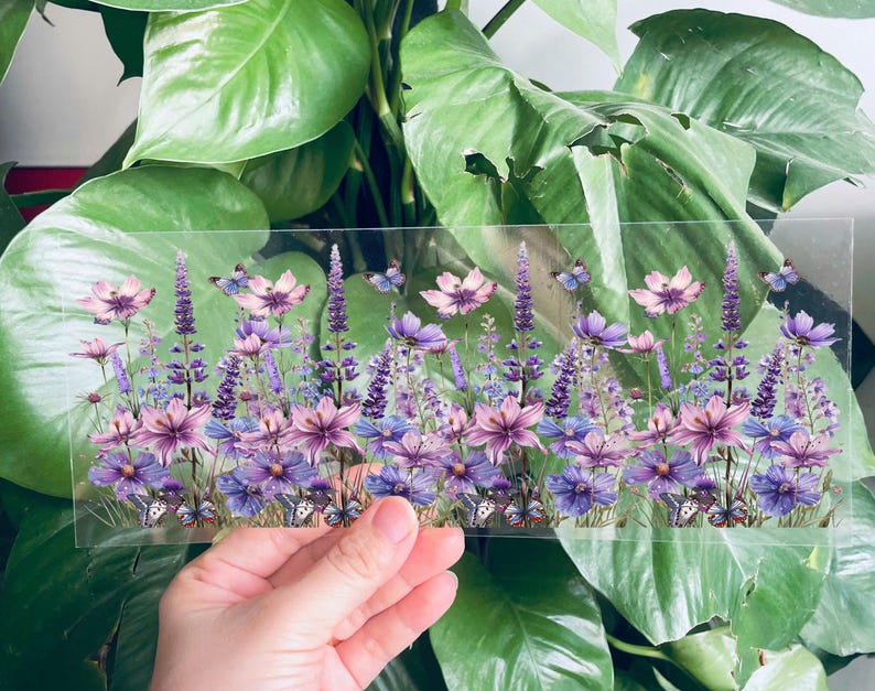 Puede incluir: Una l&aacute;mina transparente de vinilo con un dise&ntilde;o impreso de flores moradas y rosas y mariposas. Las flores est&aacute;n dispuestas en fila y las mariposas est&aacute;n dispersas por todo el dise&ntilde;o.