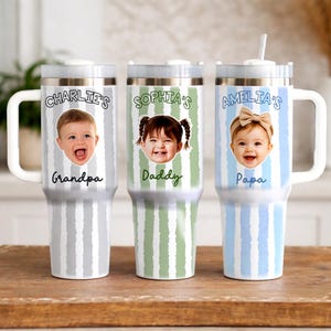 K&ouml;nnte beinhalten: Drei personalisierte Becher mit wei&szlig;en Griffen und Deckeln. Jeder Becher zeigt ein Kinderfoto und einen Namen mit dem Text "Charlie's Grandpa", "Sophia's Daddy" und "Amelia's Papa". Die Becher haben vertikal gestreifte Hintergr&uuml;nde in Grau, Gr&uuml;n und Blau.